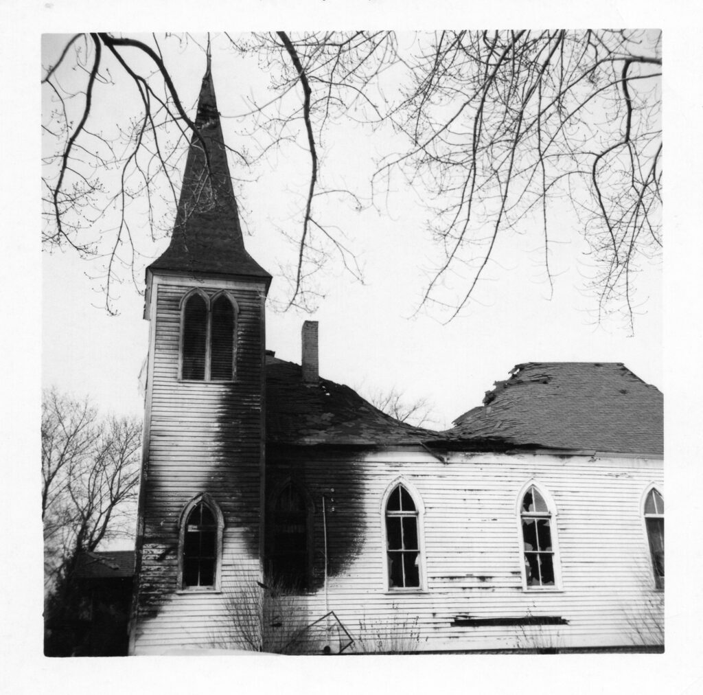 A side view of a white classically styled church building that has had the main roof collapse due to fire.